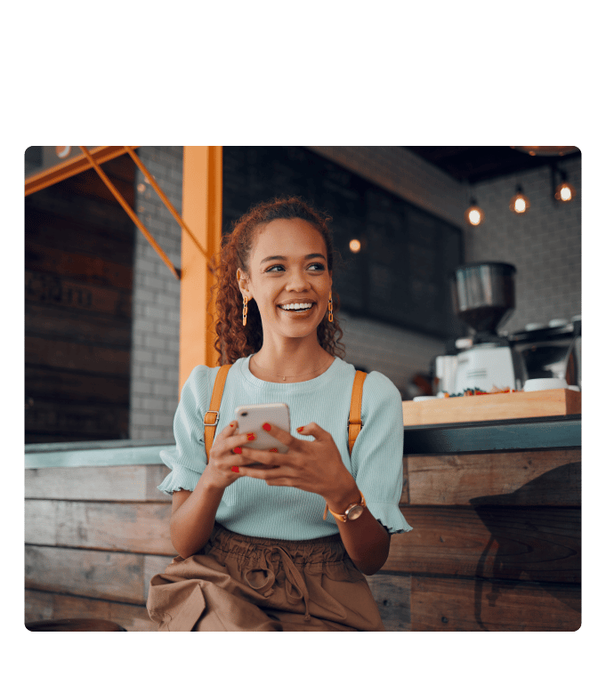 Smiling woman holding a smartphone while sitting at a café counter.