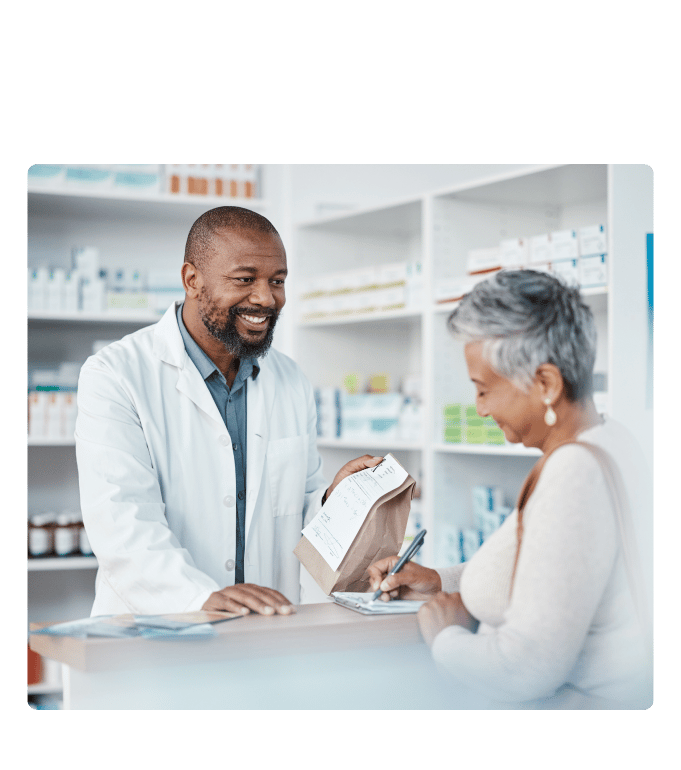 Pharmacist holds a paper bag while a person signs a form at a pharmacy counter