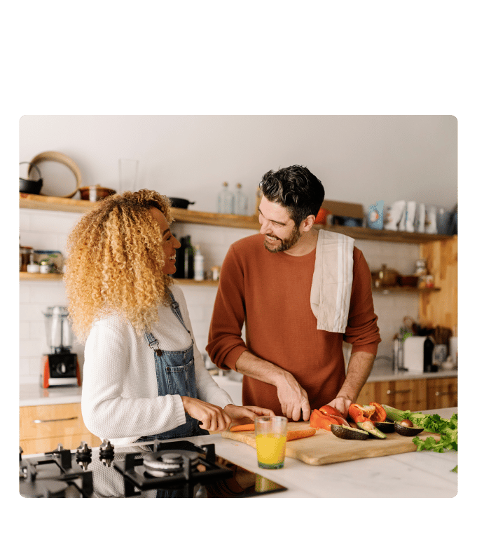 Two people chop vegetables together at a kitchen counter with a glass of orange juice nearby
