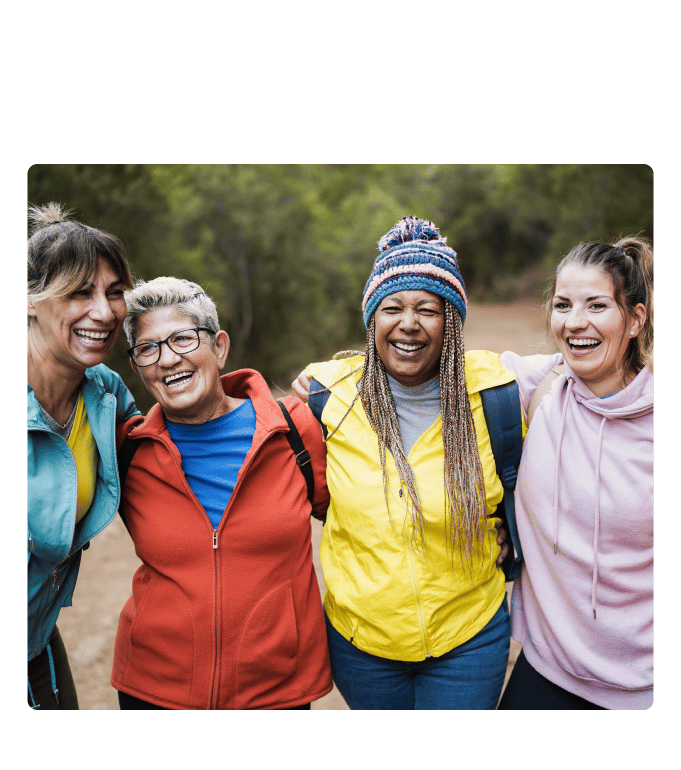 Four older women people in colorful jackets stand arm in arm on an outdoor trail
