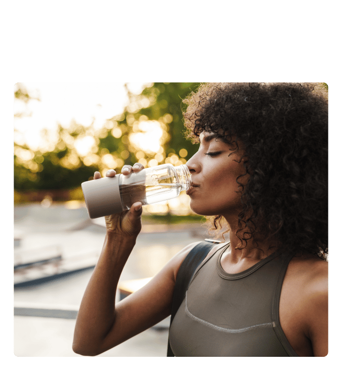 Person in workout clothes drinks from a water bottle outdoors at sunset