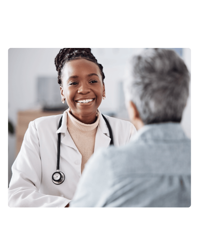Smiling doctor in a white coat and stethoscope talks with a person across a bright office