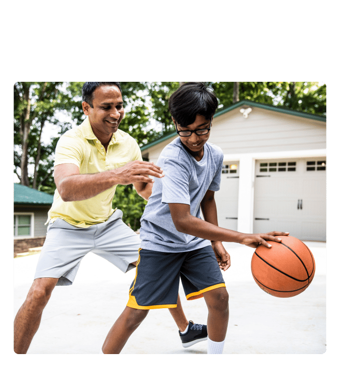 Two people play basketball on a driveway in front of a garage