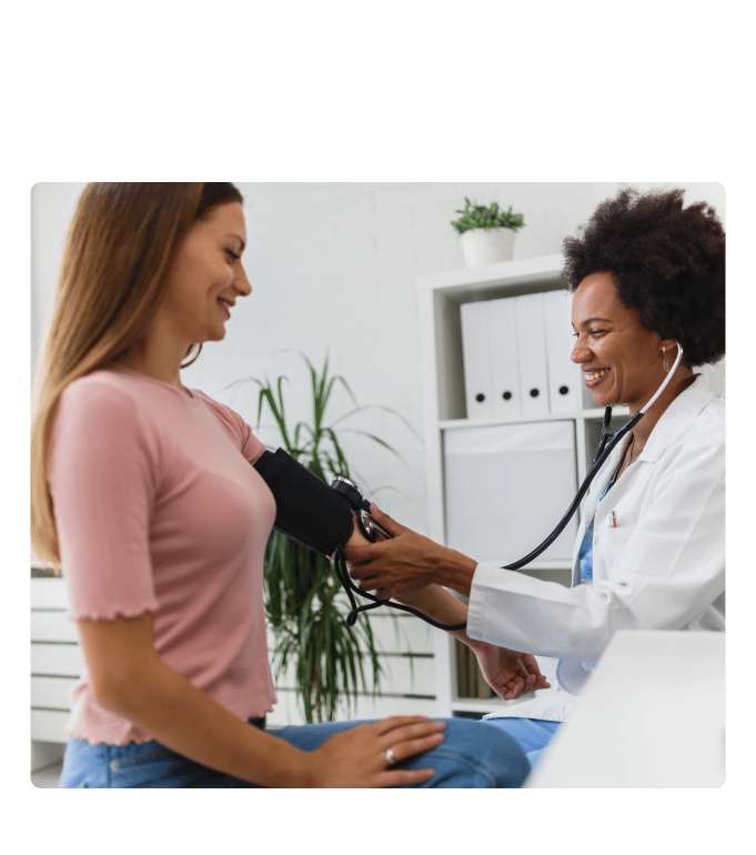 Smiling provider in a white coat takes a seated person's blood pressure in a bright office