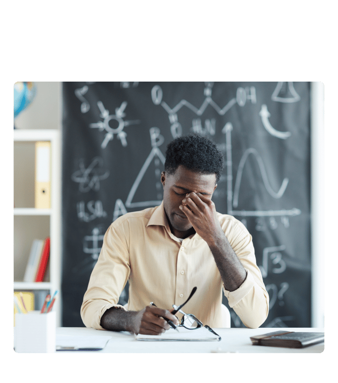 Person at a desk pinches the bridge of their nose in front of a chalkboard with diagrams