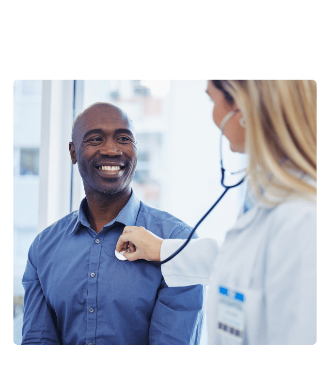 Provider listens with a stethoscope to the chest of a smiling person in a blue shirt