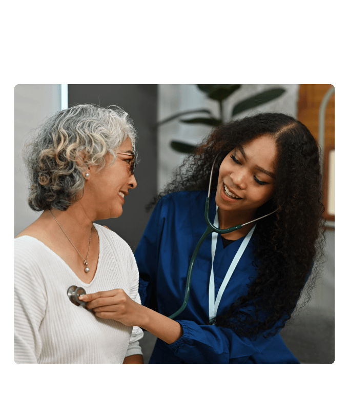 Provider in blue scrubs listens with a stethoscope to a smiling person's chest