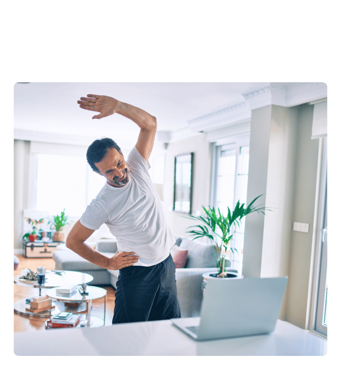Person does a standing side stretch beside a laptop in a bright living room