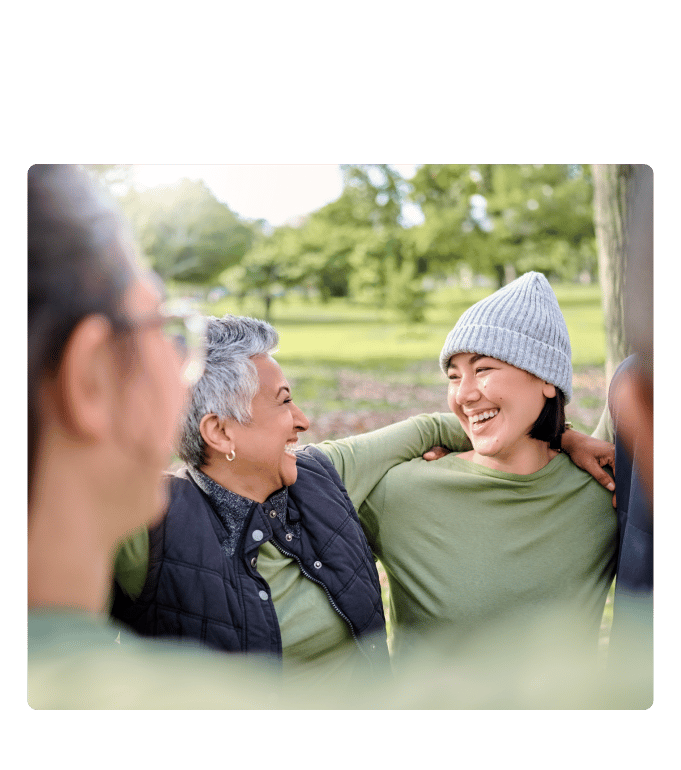 Two people in knit hats laugh together with friends in a park