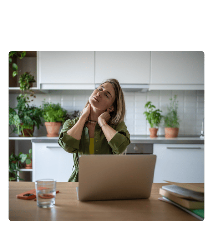 Person at a kitchen table stretches their neck with eyes closed beside a laptop