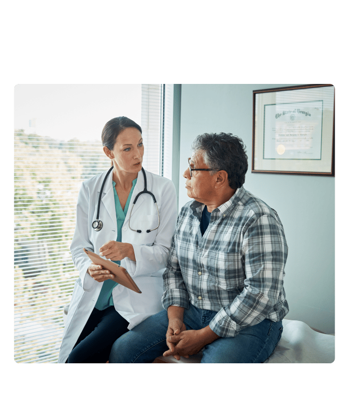 Healthcare provider with a tablet talks with a person in a plaid shirt seated in an exam room